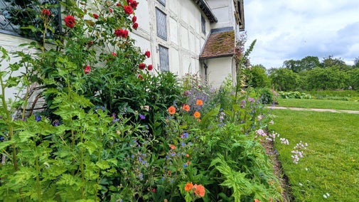 Colourful flowers in a packed cottage garden bed in front of a timbered manor house